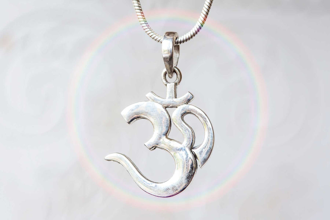 Close-up of a silver Om pendant on a necklace, with a soft rainbow halo in the background symbolizing spiritual energy and unity.
