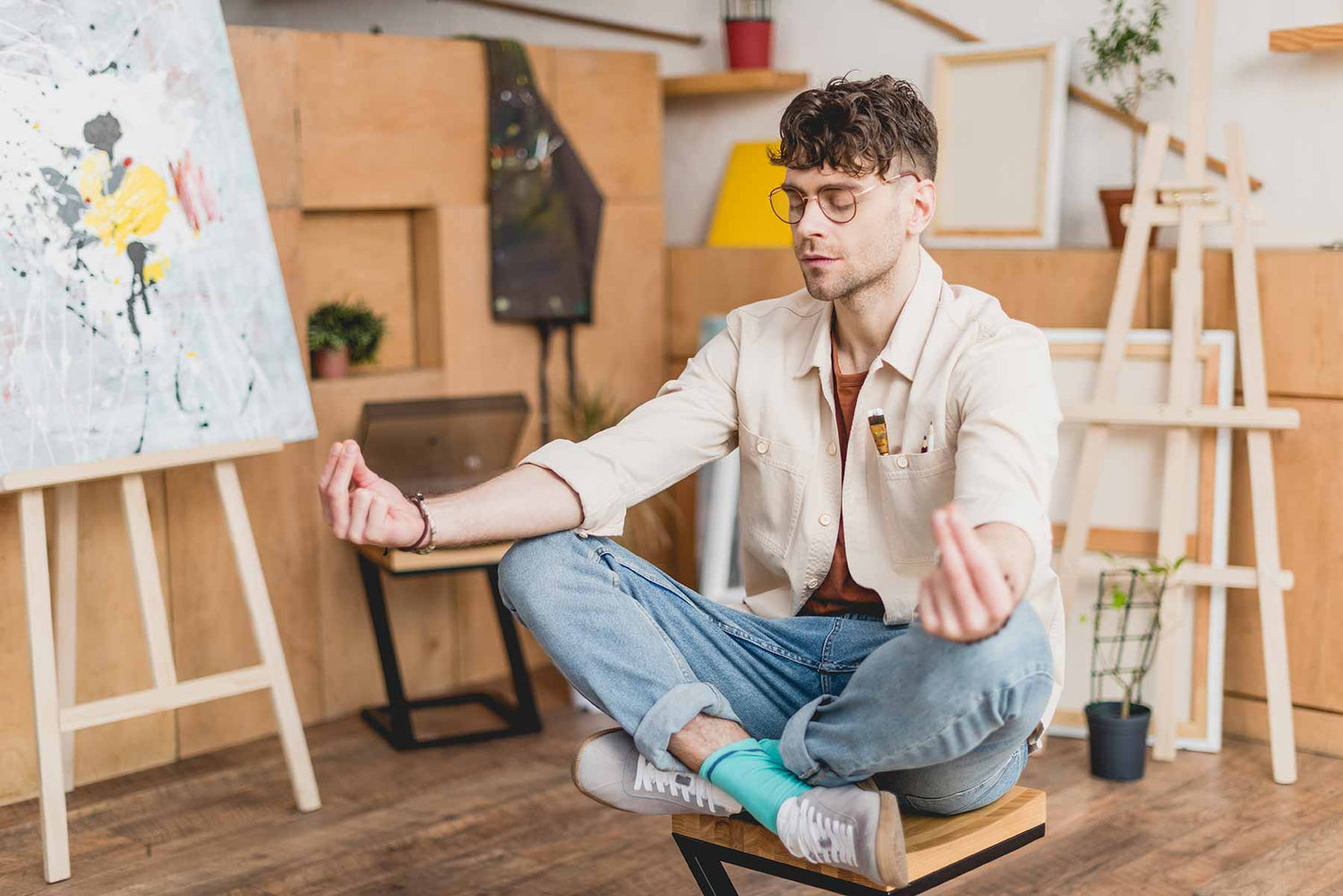 Artist sits in mindful meditation next to an unfinished painting.