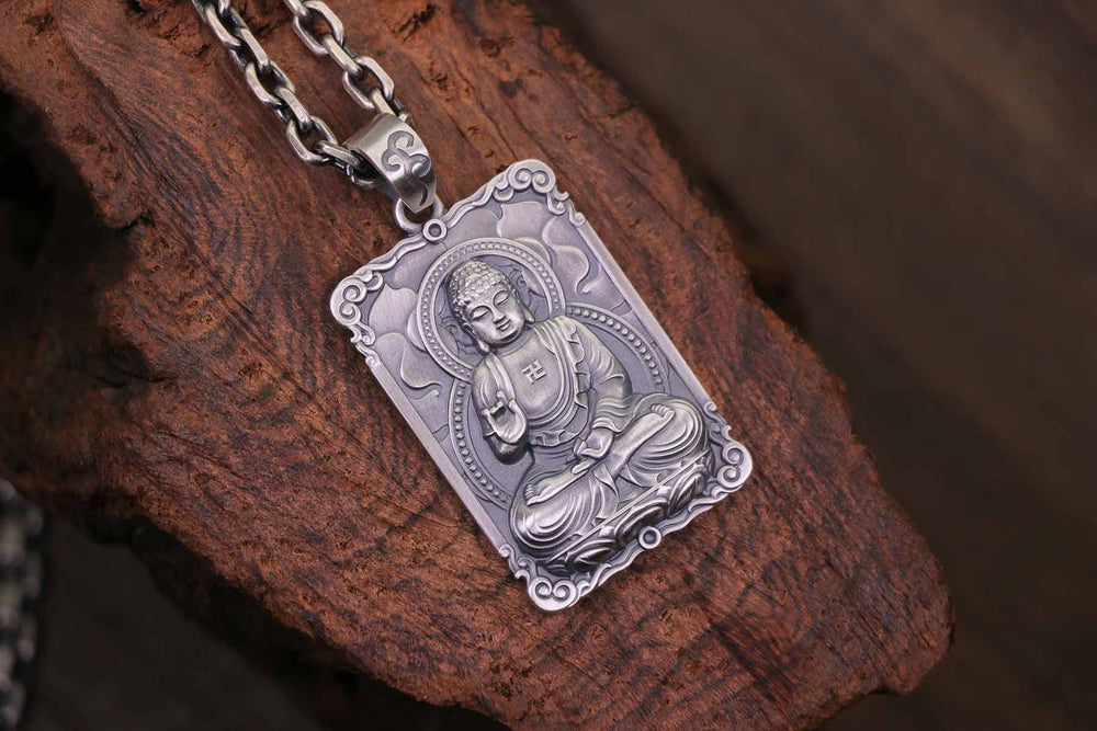 A framed silver pendant with a seated Buddha engraving and auspicious symbol, resting on wood.