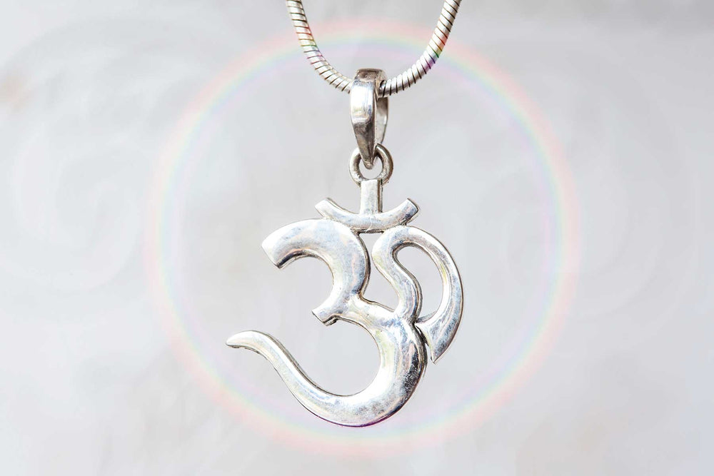 Close-up of a silver Om pendant on a necklace, with a soft rainbow halo in the background symbolizing spiritual energy and unity.
