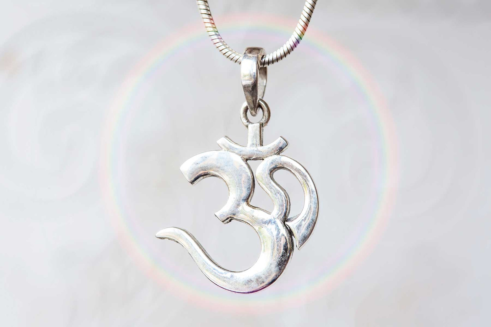 Close-up of a silver Om pendant on a necklace, with a soft rainbow halo in the background symbolizing spiritual energy and unity.