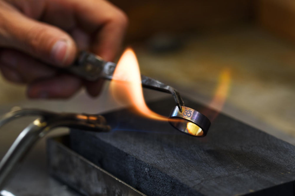 An artisan carefully heats a metal ring engraved with the Om symbol.