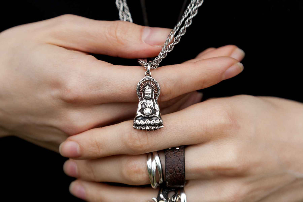 Close-up of hands holding a silver Buddhist pendant shaped like a serene, seated figure.