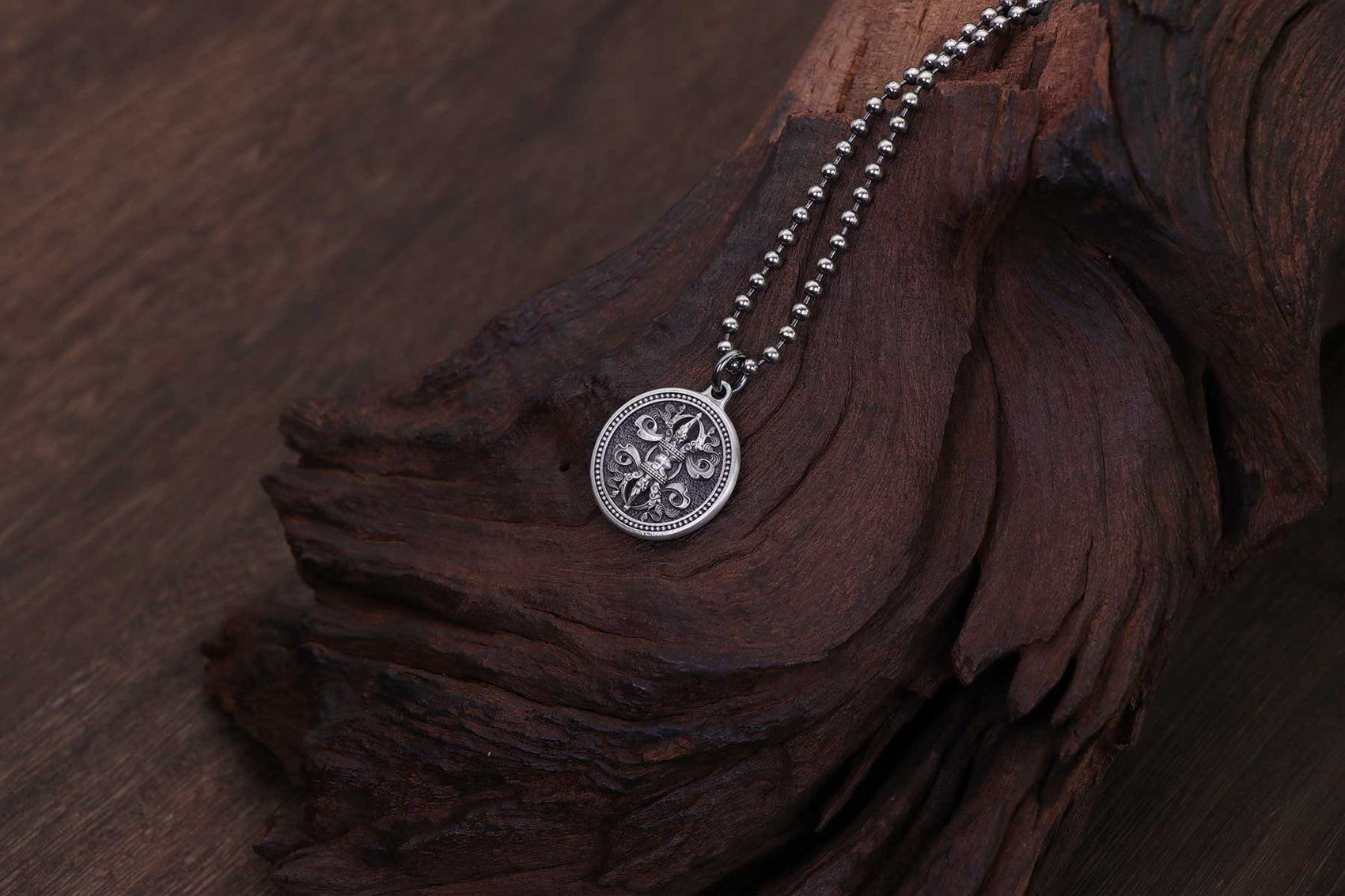 A silver Vajra pendant on a beaded chain rests on a piece of dark, weathered wood. The detailed design symbolizes spiritual strength, clarity, and protection, highlighting the pendant’s deep-rooted meaning in ancient traditions.