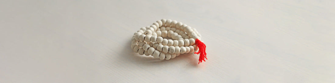 White tulsi mala beads with red tassel on a white wooden board