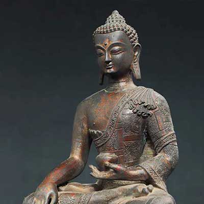 Bronze statue of a seated Buddha with intricate details on a dark background